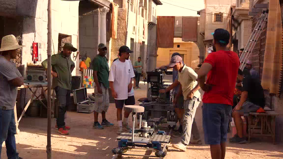 Lieu de tournage à Marrakech : ruelle de ksar transformée en plateau, avec chariot de travelling sur rails et équipe technique