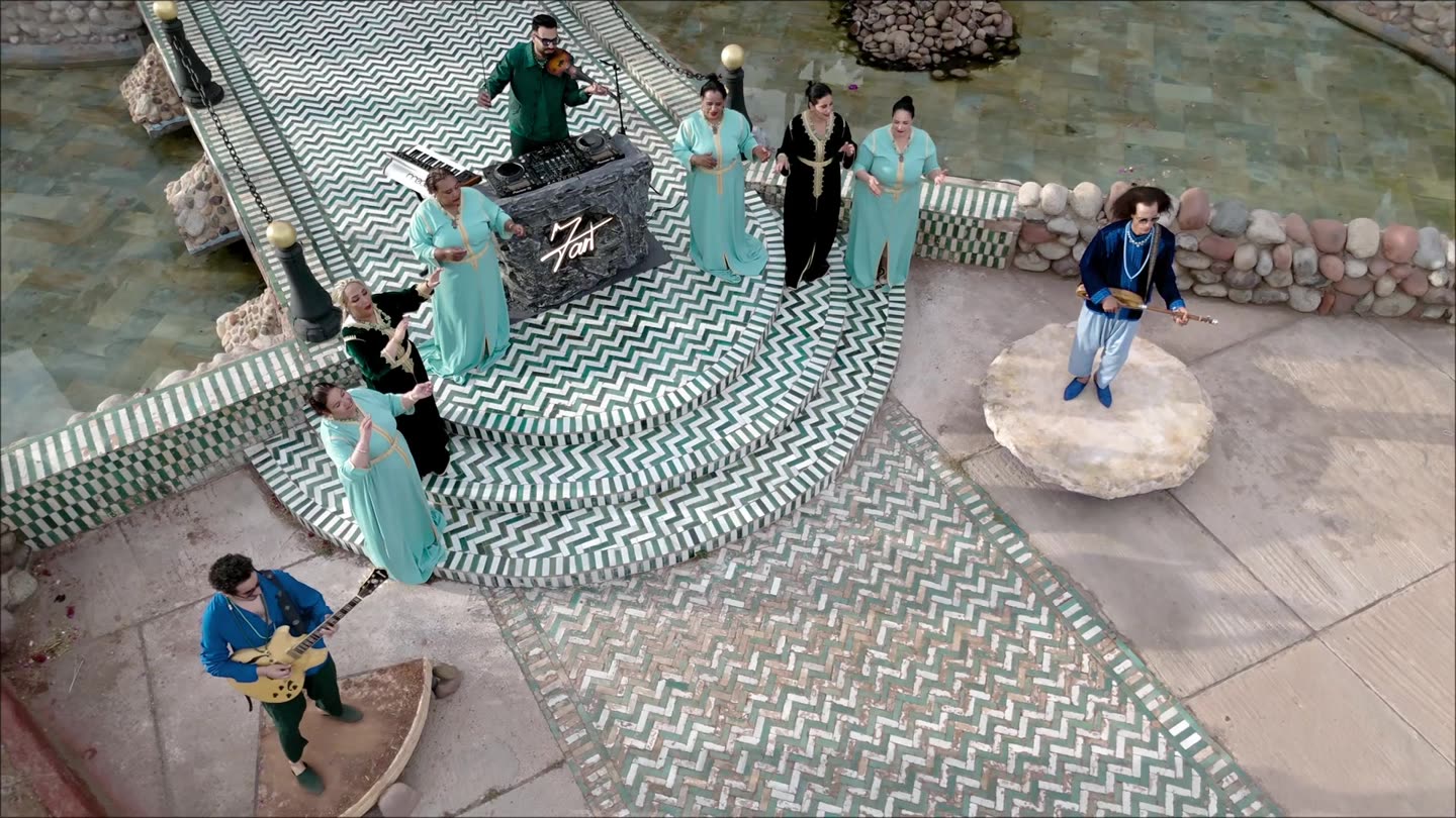 Vue aérienne d'un décor de palais marocain pendant le tournage d'un clip : musiciens et choristes disposés sur un sol en zellige