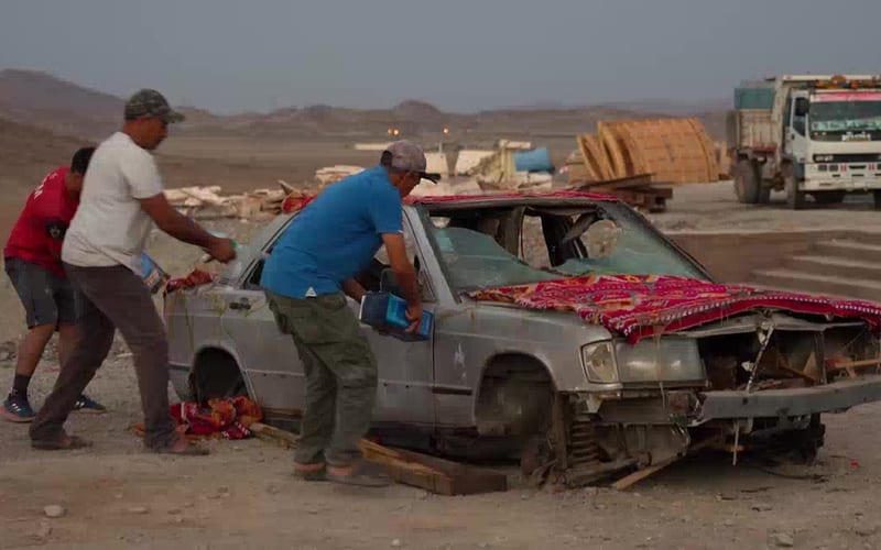 Équipe préparant un véhicule de décor dans le désert marocain, camion et matériel en arrière-plan