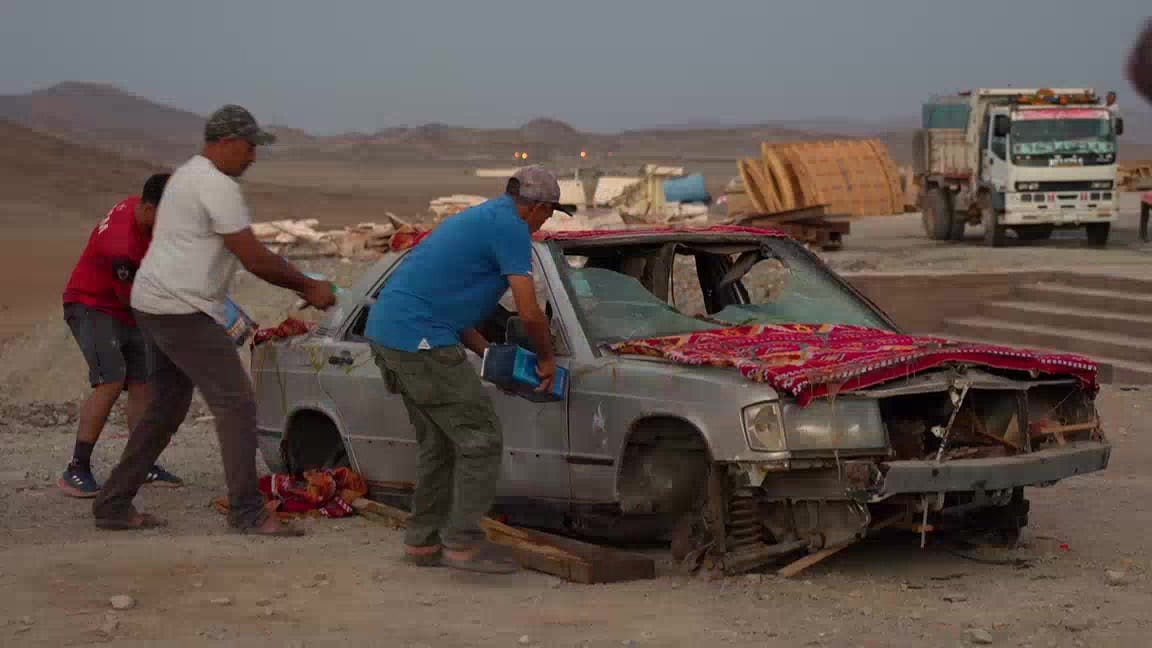 Équipe préparant un véhicule de décor dans le désert marocain, camion et matériel en arrière-plan